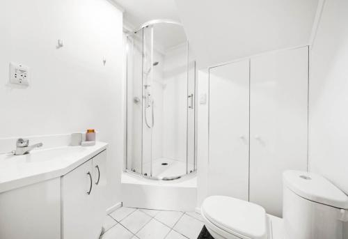 a white bathroom with a shower and a toilet at Spacious 3-Bedroom Retreat Near Airport & City in Auckland