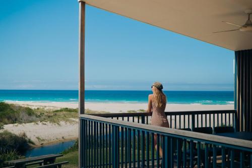 Una mujer parada en un balcón con vistas a la playa en BIG4 Tasman Holiday Parks - Racecourse Beach, en Bawley Point