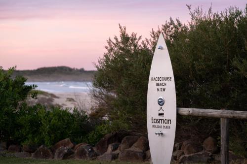 a white surfboard leaning against a fence next to a beach at BIG4 Tasman Holiday Parks - Racecourse Beach in Bawley Point