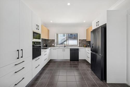 a kitchen with white cabinets and a black refrigerator at Galoola Hidden Gem, 2-97 Galoola Drive, Rooftop outdoor area with spectacular views, Wi-Fi, Air Conditioning, Pet Friendly in Nelson Bay