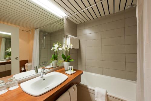 a bathroom with a sink and a bath tub with a mirror at Mercure Hotel Hamburg am Volkspark in Hamburg
