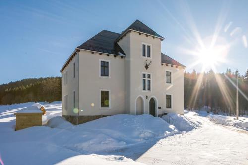 a house in the snow with the sun behind it at Alte Försterei Wildenthal in Eibenstock