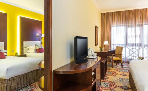 a hotel room with two beds and a desk with a tv at Coral Dubai Deira Hotel in Dubai