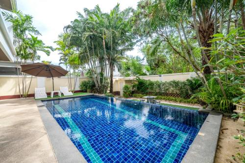 an outdoor swimming pool with an umbrella and trees at Pattaya Private 4-Bedrooms, 5-Bathrooms Pool Villa in Jomtien Beach