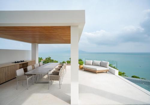 eine Außenterrasse mit einem Tisch, Stühlen und Meerblick in der Unterkunft Cape Azure Resort Samui by Thalsea in Plai Laem