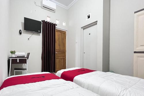 a bedroom with two beds and a tv on the wall at RedDoorz Syariah Omah Audrey near RSI Kota Magelang in Kedungsari
