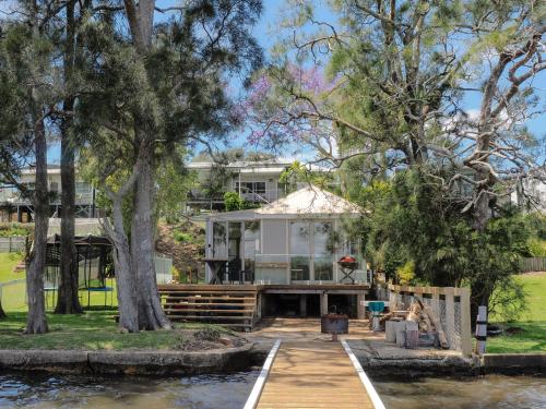 ein Haus am Wasser mit Bäumen und einem Steg in der Unterkunft Jerrinja - Absolute waterfront with jetty - 5 mins to Hyams Beach in Erowal Bay