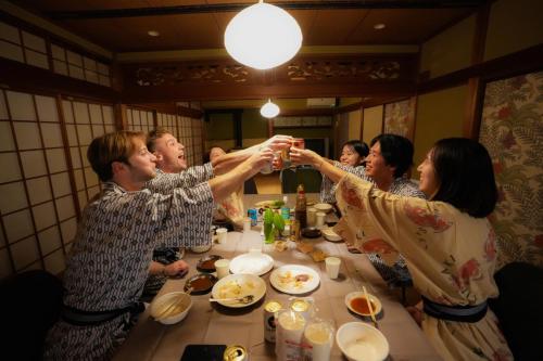 Eine Gruppe von Menschen, die um einen Tisch sitzen und Hände schütteln. in der Unterkunft Base House Kinosaki - Vacation STAY 68122v in Tsuiyama