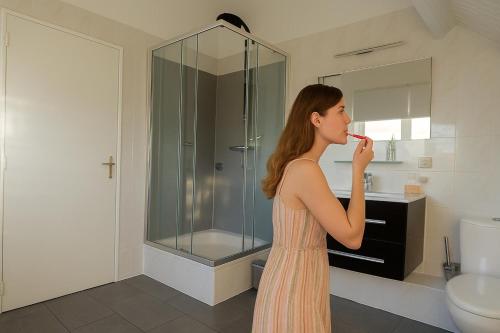 una donna che si lava i denti in un bagno di Traumhaftes-freistehendes-Ferienhaus-an-der-See-Strand-Yachthafen-W-Lan a Bruinisse