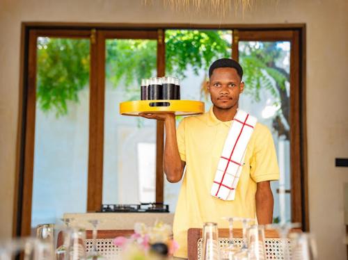 Ein Mann hält einen Teller auf einem Tisch. in der Unterkunft Tulia House Lamu in Lamu