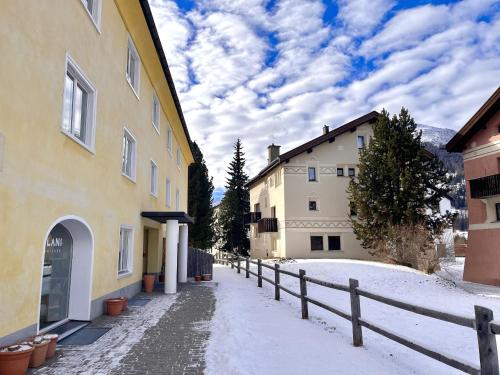 un callejón cubierto de nieve con edificios y una valla en Chesa Principela - La Punt, en La Punt-Chamues-ch