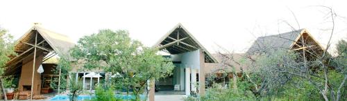 a building with two pointed roofs with trees in front at Toshari Lodge in Okaukuejo