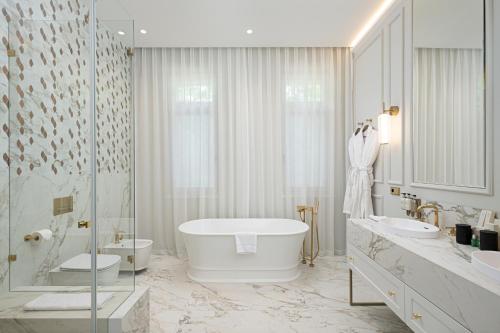 La salle de bains blanche est pourvue de 2 lavabos et d'une baignoire. dans l'établissement Avalon Luxury Villa, à Miskolc