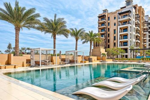 a swimming pool with palm trees and a building at Modern 1BR Apartment Lamtara 3 in MJL in Dubai