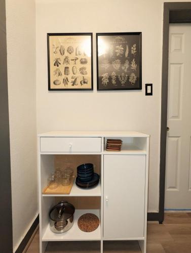a white shelf with dishes on a wall with two pictures at The Green House, RiNo in Denver