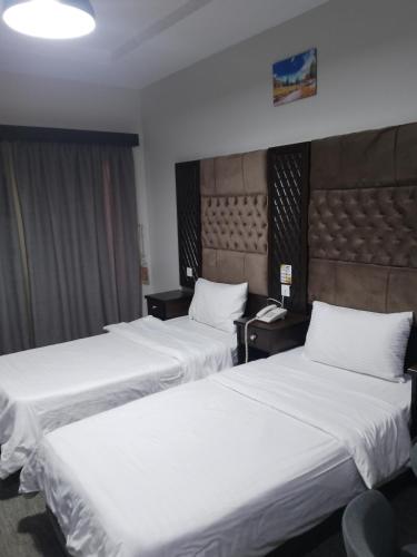 two beds in a hotel room with white sheets at Nilufer AlHada Hotel - فندق نيلوفر الهدا in Taif
