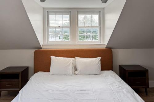 1 dormitorio con 1 cama con 2 mesitas de noche y 2 ventanas en Stowe Mountain Road Retreat, en Stowe