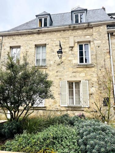 Una antigua casa de piedra con ventanas blancas y arbustos. en La vue sacrée, en Laon