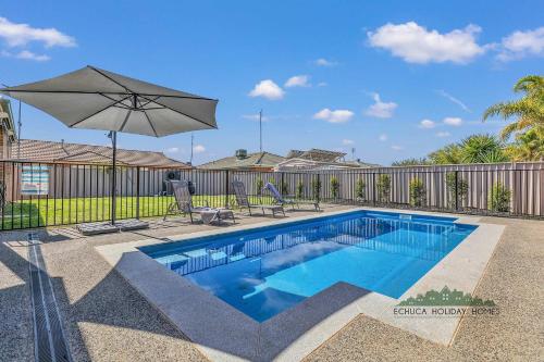 a swimming pool with an umbrella next to a fence at Central Echuca Escape, Heated Pool, 3 BDR in Echuca