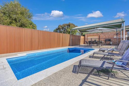 a swimming pool with two chairs and an umbrella at Central Echuca Escape, Heated Pool, 3 BDR in Echuca