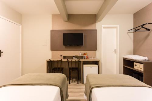 a room with two beds and a desk and a tv at Hotel Farol da Ilha in Florianópolis