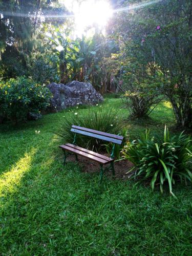 a wooden bench sitting in the grass in a park at Bangalo a beira do rio em plena natureza in Petrópolis