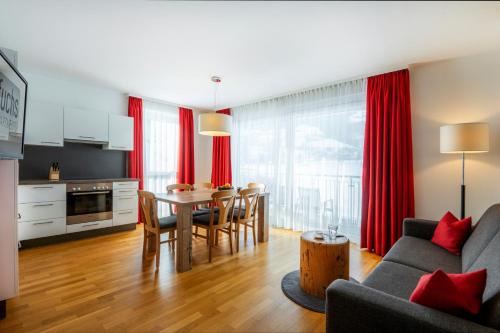 ein Wohnzimmer mit einem Tisch und eine Küche mit roten Vorhängen in der Unterkunft Fuchs Apartments - inklusive Eintritt in die Alpentherme Gastein in Bad Hofgastein