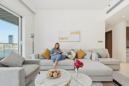 a woman sitting on a couch in a living room at Luxury 2BR Emaar Beachfront with Private Beach & Infinity Pool, Palm Jumeirah & Atlantis Views in Dubai