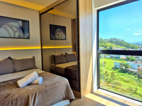 een slaapkamer met een bed en een groot raam bij CURTA! |165| Lindo Studio | Próx Centro de Eventos in Balneário Camboriú