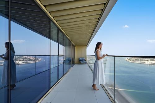 a woman in a white dress standing on a balcony looking out over the city at Luxury 2BR Emaar Beachfront with Private Beach & Infinity Pool, Palm Jumeirah & Atlantis Views in Dubai