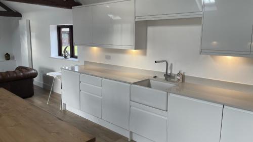 a kitchen with white cabinets and a sink at Eastfields Farm Barns in Melchbourne
