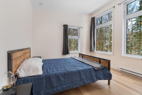a bedroom with a blue bed and two windows at Le 4 sur le lac, Accès au lac, Boisée, BBQ in Wentworth