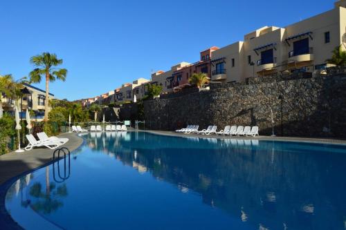 a large swimming pool with white chairs and buildings at Gurugu Beach House in Palm-Mar