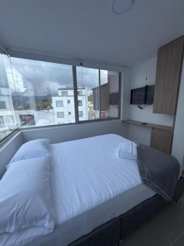 Cama blanca en habitación con ventana grande en hotel portal del cerro manizalez, en Manizales