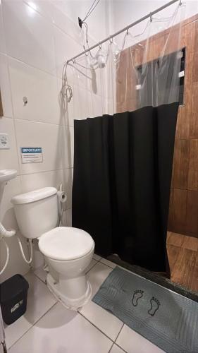 a bathroom with a toilet and a black shower curtain at SUÍTES PÉ na AREIA ANGRA in Angra dos Reis