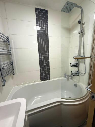 eine weiße Badewanne mit einer schwarz gefliesten Dusche in der Unterkunft Wigan 2-Bedroom Modern house - Cozy & Relaxing Stay in Bickershaw
