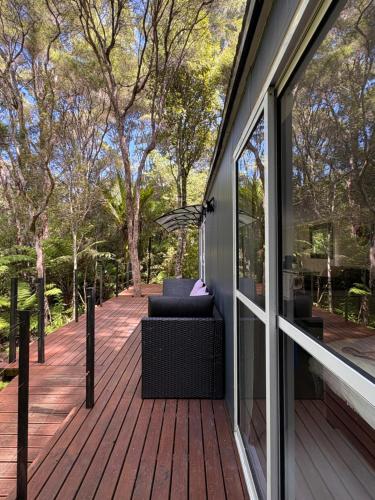Una terraza de madera con un sofá al costado de una casa. en Tui Bush Chalet, en Parakakau