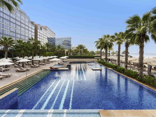 a pool with chairs and umbrellas and palm trees at Fairmont Bab Al Bahr in Abu Dhabi