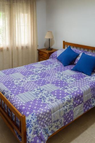casa super comoda para 6 personas Miramar في ميرامار: سرير مع لحاف أرجواني ووسائد زرقاء