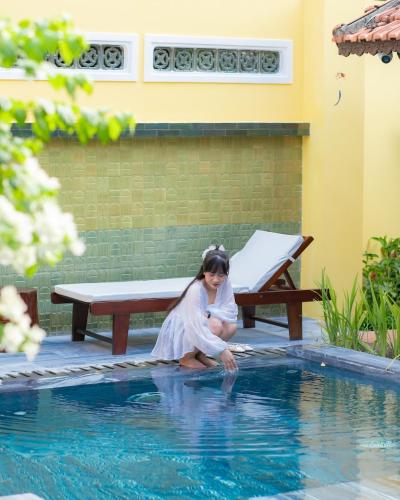 a young girl sitting on the edge of a swimming pool at DEMIN VILLA HỘI AN - POOL & BBQ Gaden in Hoi An