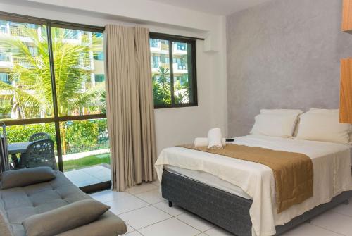 a bedroom with a bed and a couch and a window at Mana Beach Experience B019 in Porto De Galinhas