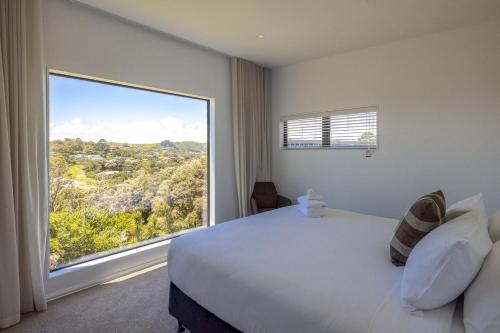 a bedroom with a large bed and a large window at Hidden Valley Waiheke in Palm Beach
