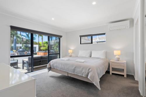 a white bedroom with a bed and a large window at Beach Escape Papamoa in Papamoa
