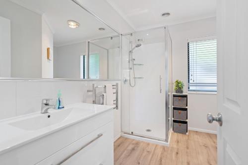 a white bathroom with a sink and a shower at Beach Escape Papamoa in Papamoa