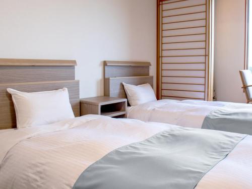 a bedroom with two beds with white sheets at KAMENOI HOTEL Aomori Makado in Noheji