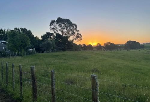 een hek in een veld met de zonsondergang op de achtergrond bij Gordonton Greenmeadows Cottage in Taupiri