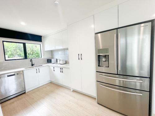 a kitchen with white cabinets and a stainless steel refrigerator at Brand-New 5BR Retreat, Space & Serenity by Nature in Auckland