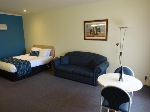 a hotel room with a bed and a couch and a chair at Victoria Lodge Motor Inn & Apartments in Portland