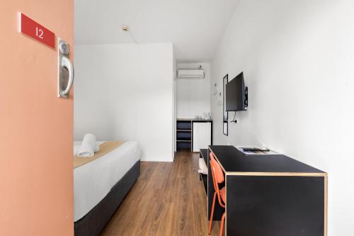 a small room with a bed and a desk with a tv at The Palms Motel- Formerly Flinders Motel in Wollongong