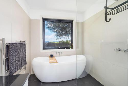 a white bathroom with a tub and a window at Farmhouse on the Cradle Coast Forth in Forth